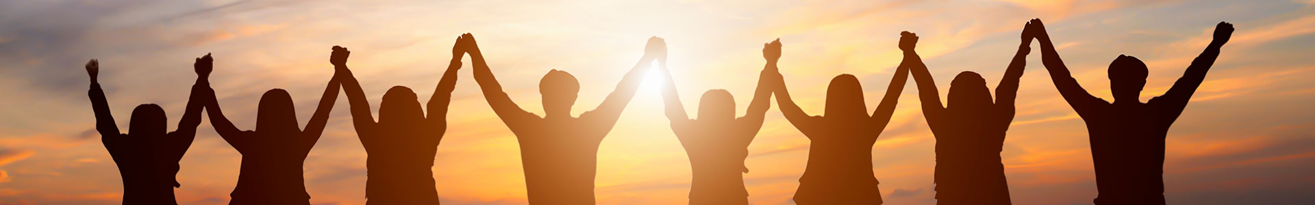Stock image of people with joined hands overhead, silhouetted by a sunset.